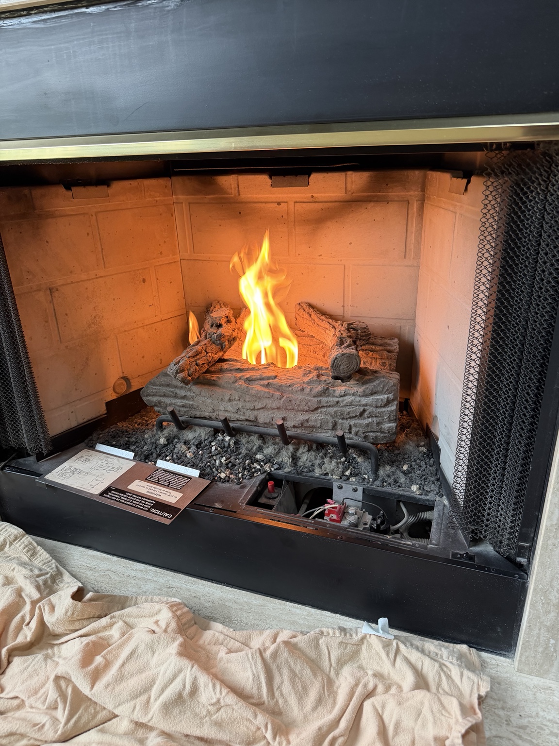 Gas log fireplace lit during a service visit, with controls accessible and a protective cloth on the floor